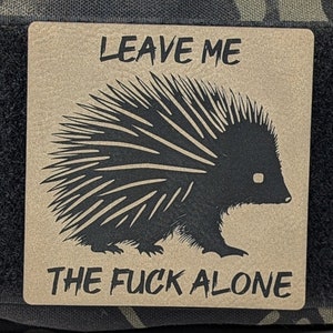 May include: A brown patch with a black silhouette of a porcupine and the text "LEAVE ME THE FUCK ALONE".
