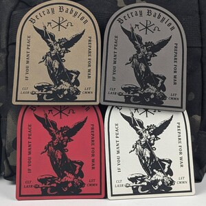 May include: Four embroidered patches with a black and white image of an angel trampling a demon. The patches are beige, gray, red, and white. The text on the patches reads "Betray Babylon", "If you want peace, prepare for war", "CLT LASR", and "LST CMMN".
