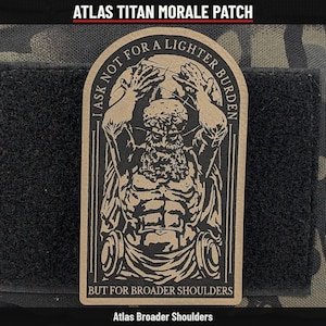 May include: A tan and black morale patch featuring a graphic of Atlas holding a globe above his head. The text reads I ASK NOT FOR A LIGHTER BURDEN BUT FOR BROADER SHOULDERS. The patch has a rounded top and is attached to a black hook-and-loop fastener.