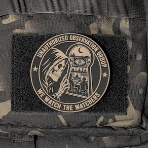 May include: A circular black and tan morale patch featuring a hooded skeleton looking through a keyhole at a surveillance room with multiple screens and an eye symbol. The text reads UNAUTHORIZED OBSERVATION GROUP and WE WATCH THE WATCHERS.