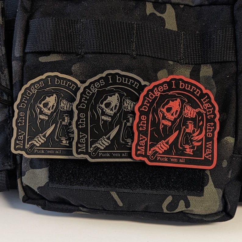 May include: Three patches with a grim reaper design. The patches are black, tan, and red, with the text "May the bridges I burn" and "Fuck 'em all". The red patch also says "light the way".