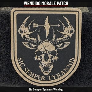 May include: A tan and black morale patch featuring a central deer skull with large antlers. Above the skull is a horizontal arrow and a lightning bolt. The text "SIC SEMPER TYRANNIS" is printed in a curved arc along the bottom edge.