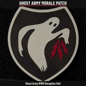 May include: A shield-shaped morale patch featuring a white ghost graphic on a black background with three red lightning bolts. The text GHOST ARMY MORALE PATCH and Ghost Army WWII Deception Unit are printed in white at the top and bottom.