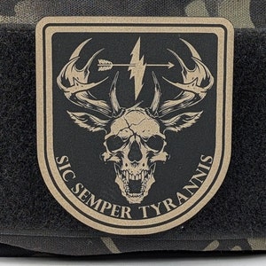 May include: A tan-colored patch with a black background featuring a skull with antlers, a lightning bolt, and an arrow. The text "SIC SEMPER TYRANNIS" is written around the skull.