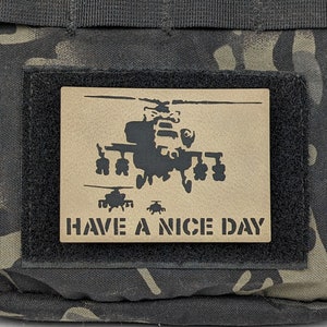 May include: A tan-colored patch with a black silhouette of a helicopter and three smaller helicopters flying behind it. The text "HAVE A NICE DAY" is printed below the helicopters.