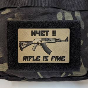 May include: A tan patch with black text and a black and white illustration of a rifle. The text reads "ИЧET !! RIFLE IS FINE".