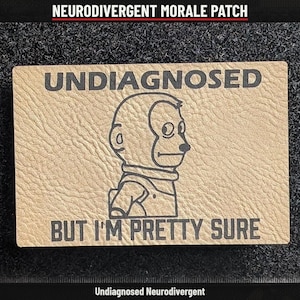 May include: A rectangular tan morale patch with a textured surface featuring a black line drawing of a monkey looking sideways. The text UNDIAGNOSED is printed above the monkey, and the text BUT I'M PRETTY SURE is printed below it.
