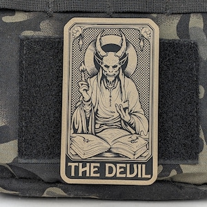 May include: A brown card with a black and white illustration of a devil holding a torch and a book. The card has the text "THE DEVIL" at the bottom.