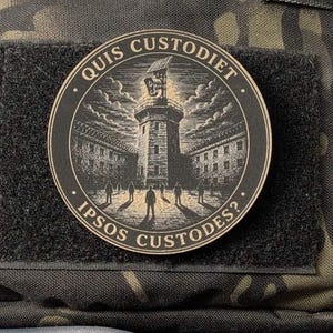 May include: A circular black and tan morale patch featuring an engraved illustration of a central tower with a spotlight, surrounded by silhouettes of people. The text "QUIS CUSTODIET IPSOS CUSTODES?" is inscribed along the circular border.