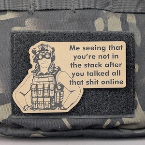 May include: A tan patch with a female soldier illustration and the text "Me seeing that you're not in the stack after you talked all that shit online." The patch is attached to a black velcro square on a camouflage background.