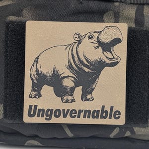 May include: A brown patch with a black and white illustration of a hippopotamus with its mouth open. The patch has the text "Ungovernalbe" printed in black letters.