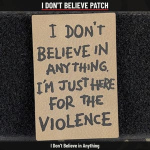 May include: A rectangular tan morale patch with black text that reads, I DON'T BELIEVE IN ANYTHING. I'M JUST HERE FOR THE VIOLENCE. The patch is centered on a black hook-and-loop fastener backing, featuring a matte finish and bold lettering.