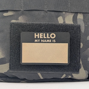 May include: A black velcro patch with a black name tag that says "HELLO MY NAME IS" with a blank space for a name.