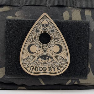 May include: A brown, triangular-shaped ouija board with a black and white illustration of an eye, wings, and the words "YES", "NO", "HELLO", and "GOOD BYE".