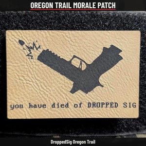May include: A rectangular tan morale patch with a textured surface featuring a black silhouette of a handgun firing a bullet. The text "you have died of DROPPED SIG" is printed in black at the bottom of the patch in a pixelated font.