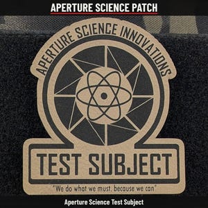 May include: A tan and black patch featuring the text Aperture Science Innovations in an arc above a central atom symbol and camera aperture graphic. Below this, the text TEST SUBJECT appears with the quote We do what we must, because we can.