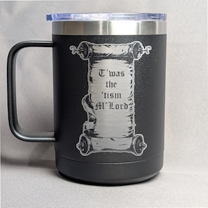 May include: Black travel mug with a silver rim and handle. The mug features a scroll design with the text "T'was the 'tism M'Lord" etched on the front. The mug has a clear plastic lid.