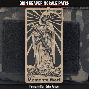 May include: A rectangular morale patch featuring a tan and black graphic of a hooded skeleton figure holding a rifle and a scythe. The design includes sunburst rays in the background and the text Memento Mori at the bottom of the patch.