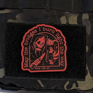 May include: A red patch with a grim reaper design holding a lantern and knife, with the text "May the bridges I burn light the way" and "Fuck 'em all" on a black background.