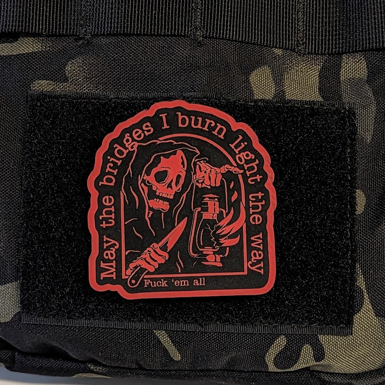 May include: A red patch with a grim reaper design holding a lantern and knife, with the text "May the bridges I burn light the way" and "Fuck 'em all" on a black background.