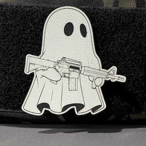 May include: A white ghost patch with a black outline, holding a black and gray rifle. The ghost has two black oval eyes. The patch is on a black, textured background.
