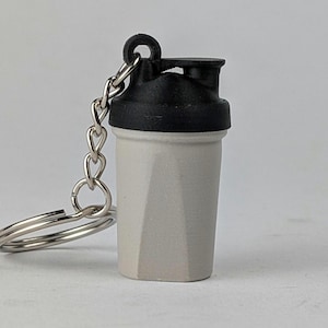 May include: A white and black shaker bottle keychain. The bottle has a black lid and a silver chain.