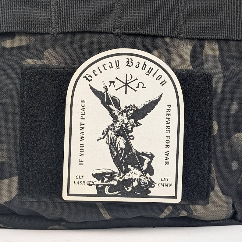 May include: A black and white patch with an angel holding a spear and a demon lying beneath it. The patch has the text "Betray Babylon" at the top, "If you want peace" on the left, and "Prepare for war" on the right. The patch also has the text "CLT LASR" on the bottom left and "LST CMNN" on the bottom right.