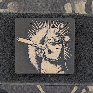 May include: A black and white illustration of a squirrel holding a gun. The squirrel is depicted in a cartoon style with a large bushy tail and a mischievous expression. The gun is a simple design with a barrel and a handle.