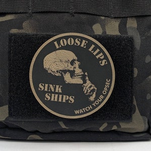 May include: A black and brown circular patch with a skull and crossbones design. The text "Loose Lips Sink Ships Watch Your Opsec" is printed around the skull.