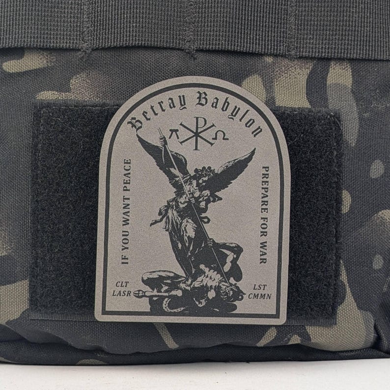 May include: A black and gray tactical bag with a patch that reads "Betray Babylon" and features an angel with a spear fighting a demon. The patch also includes the text "If you want peace prepare for war" and "CLT LASR LST CMN".