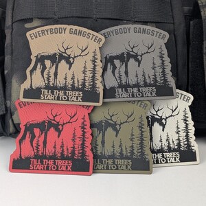 May include: Five different colored patches with a black silhouette of a moose standing in a forest. The patches have the text "Everybody Gangster" and "Till the trees start to talk" printed on them.