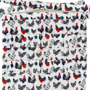 May include: White apron patterned with colourful roosters and hens. The apron has multiple pockets and a tie-around waist. The rooster and hen designs are in red, blue, black, and white.