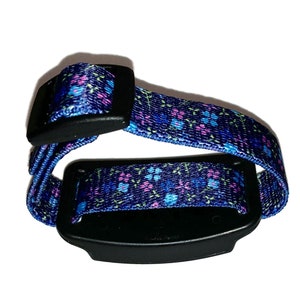 May include: A blue and pink floral patterned adjustable wristband with a black buckle and a black rectangular device attached.