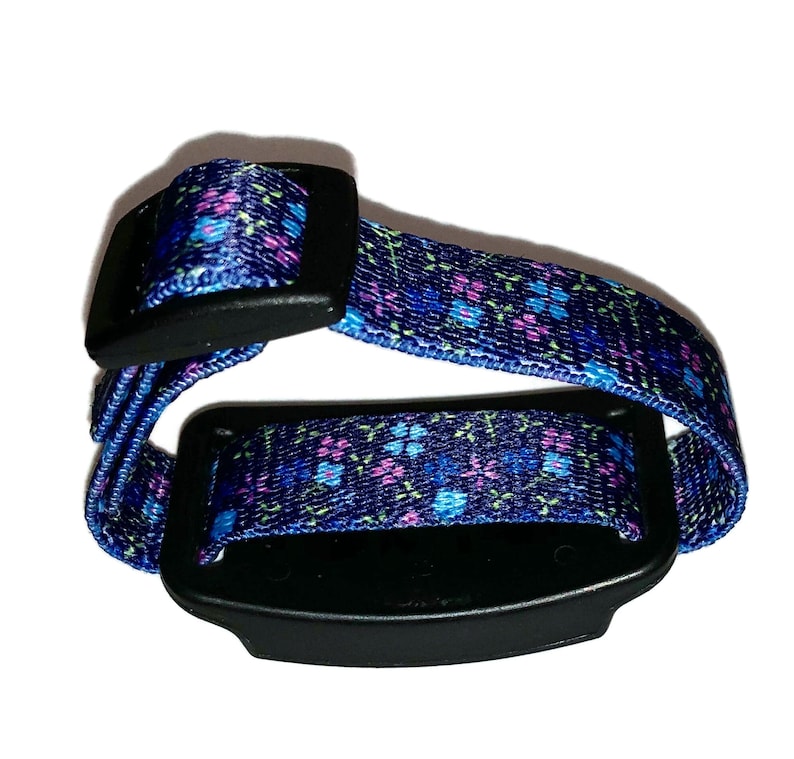 May include: A blue and pink floral patterned adjustable wristband with a black buckle and a black rectangular device attached.