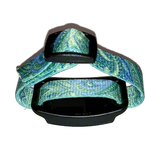 May include: A green and blue patterned adjustable wrist strap with a black buckle and a black rectangular device.