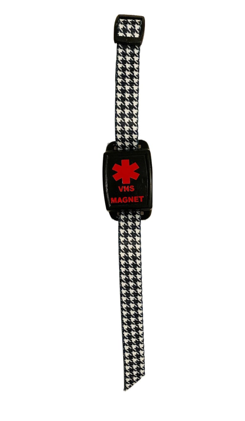 Puede incluir: Pulsera con estampado en blanco y negro con un im&aacute;n de alerta m&eacute;dica negro. El im&aacute;n tiene un s&iacute;mbolo de estrella de la vida roja y el texto "VNS MAGNET".