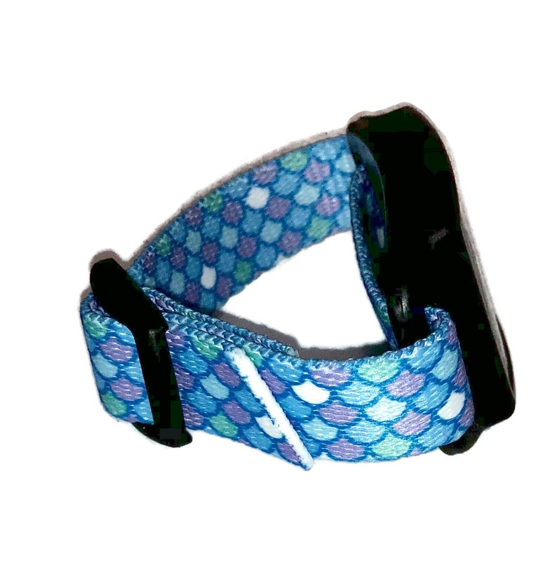 Peut inclure: Un bracelet de poignet r&eacute;glable bleu et violet avec une boucle noire. Le bracelet est en tissu et pr&eacute;sente un motif d'&eacute;cailles de sir&egrave;ne.
