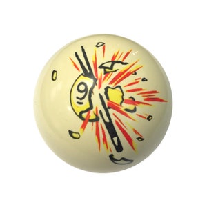 May include: A white billiard ball with a black and red graphic of a cue stick breaking through the ball with the number "9" visible. The graphic is surrounded by a yellow explosion.