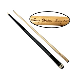 May include: Two pool cues, one black and one light wood, are displayed against a white background. The black cue has a black grip and a white tip. The light wood cue has the text "Merry Christmas Honey 2013" engraved on it.