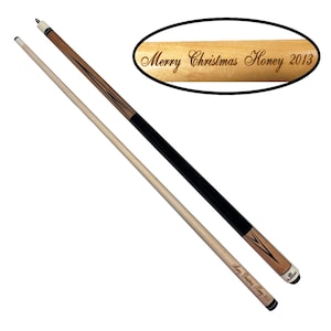 Op de afbeelding: Twee poolkeuen, één van licht hout en één zwart, met decoratieve accenten. De keu op de voorgrond heeft de tekst "Merry Christmas Honey 2013" gegraveerd. De andere keu heeft dezelfde tekst in een ovaal.