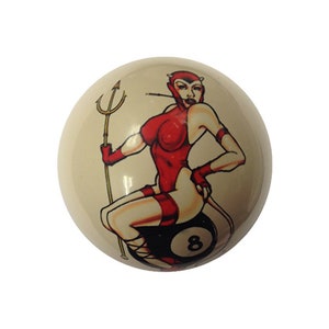 May include: A white billiard ball with a red and black illustration of a woman in a devil costume sitting on the 8 ball.