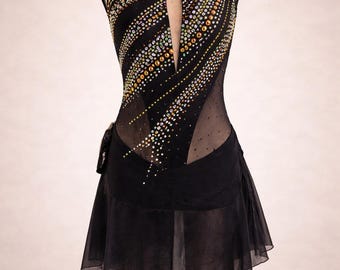 May include: Black figure skating dress with a nude mesh neckline and sleeves. The bodice features diagonal lines of colorful rhinestones. The skirt is a short, flowing black chiffon. The dress is displayed on a mannequin.
