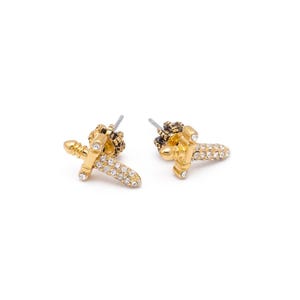 May include: A pair of gold-coloured stud earrings. Each earring is shaped like a small sword, with a handle and blade. The blade is encrusted with small, clear crystals. The top of the earring has a crown design.
