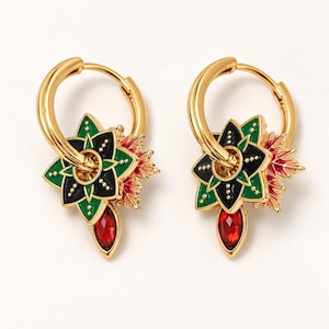 May include: A pair of gold hoop earrings featuring a multi-layered floral charm. The charm includes black and green enamel petals with gold bead accents, a red crystal drop, and a small pink and orange leaf-shaped detail on the side.