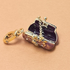 May include: A small, open, purple and gold-coloured purse with a gold chain and clasp. The purse has a decorative floral design and small crystals. The interior of the purse is a darker purple colour.