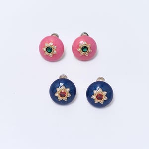 Può includere: Quattro paia di orecchini a bottone. Due paia sono rosa con una pietra centrale verde e due paia sono blu navy con una pietra centrale rossa. Ogni orecchino ha un motivo floreale dorato attorno alla pietra centrale.