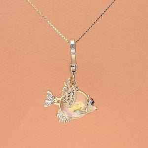 May include: Gold-toned fish pendant necklace. The pendant features a fish design with a clear body, a small tag that reads "LIMITED EDITION 2009", and crystal accents. The necklace has a delicate chain.