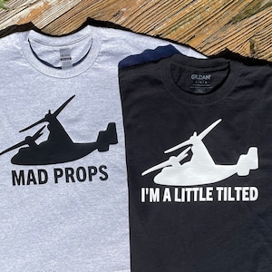 May include: Two t-shirts with a silhouette of a V-22 Osprey aircraft. The gray t-shirt has the text "MAD PROPS" and the black t-shirt has the text "I'M A LITTLE TILTED".