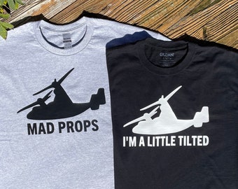 May include: Two t-shirts with a silhouette of a V-22 Osprey aircraft. The gray t-shirt has the text "MAD PROPS" and the black t-shirt has the text "I'M A LITTLE TILTED".