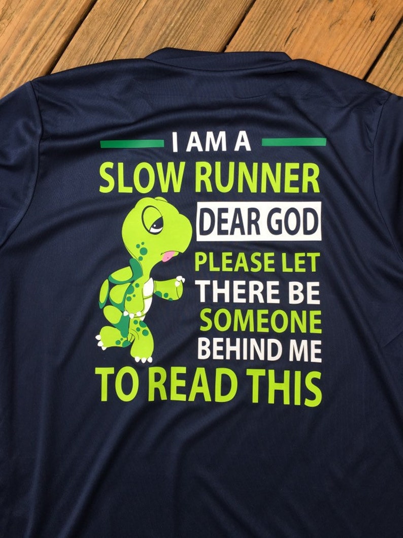 Puede incluir: Una camiseta de running azul marino con un gr&aacute;fico de tortuga verde y el texto "Soy un corredor lento. Dios m&iacute;o, por favor, que haya alguien detr&aacute;s de m&iacute; para leer esto."